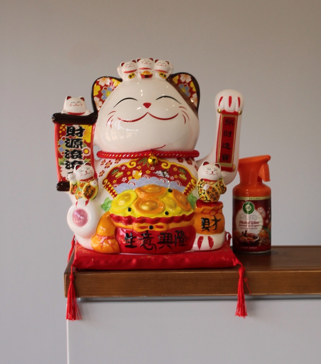 Ornate maneki-neko lucky cat figurine on a shelf, a symbol of welcome and good fortune