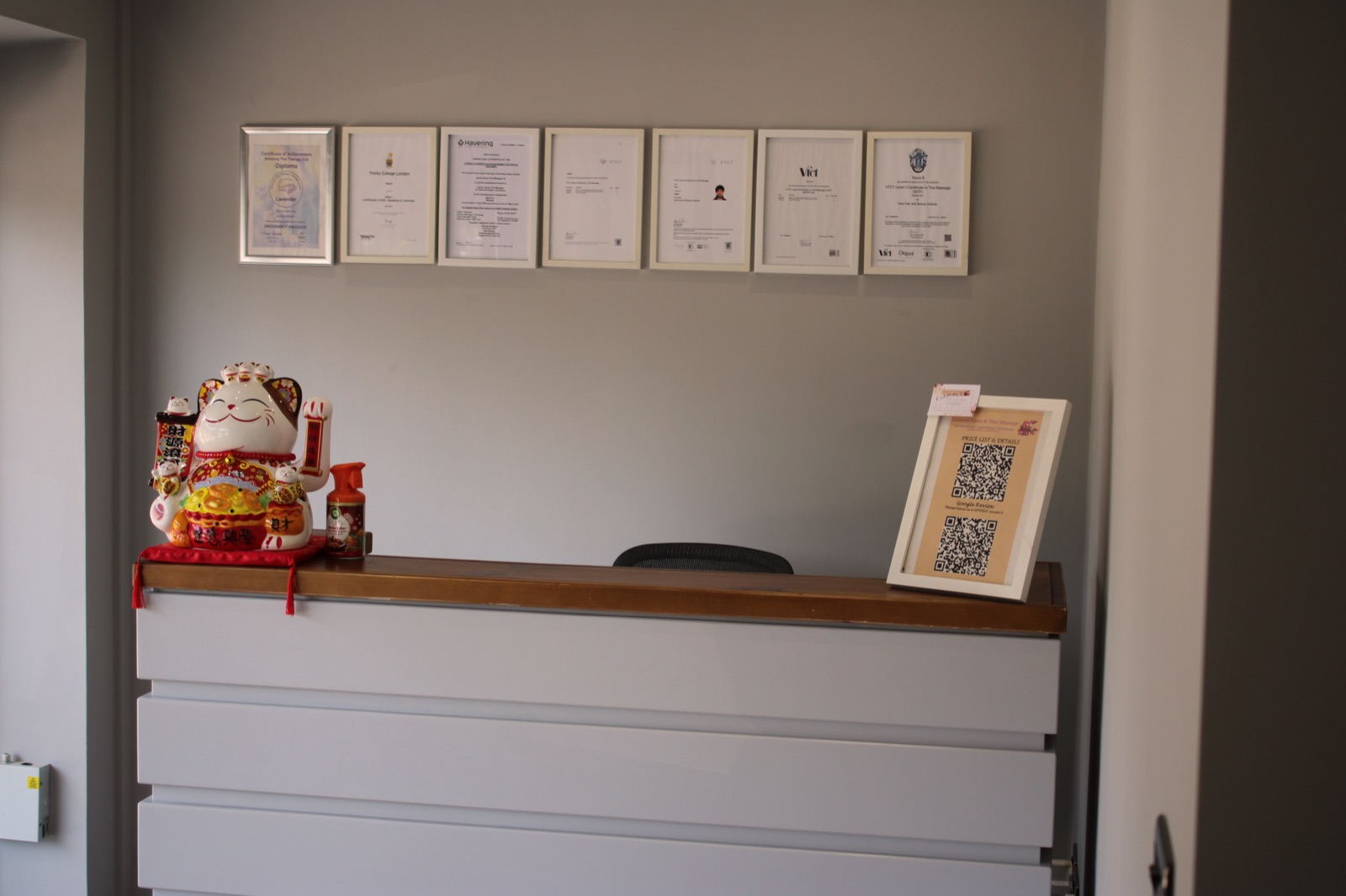 Reception desk with a wall of therapist certifications and lucky cat